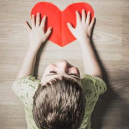 boy in green shirt holding red paper heart cutout on brown table
